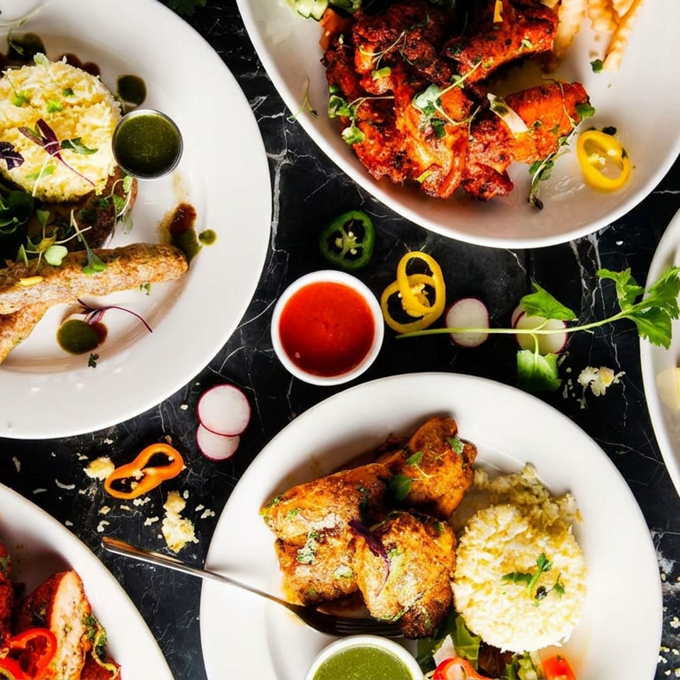 Overhead view of multiple plates of vibrant Indian dishes including chicken, kebabs, rice, and salads.